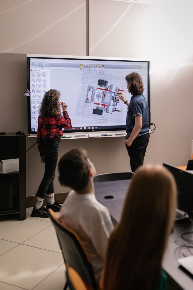 Two students presenting a robot design in simulation software on a classroom display